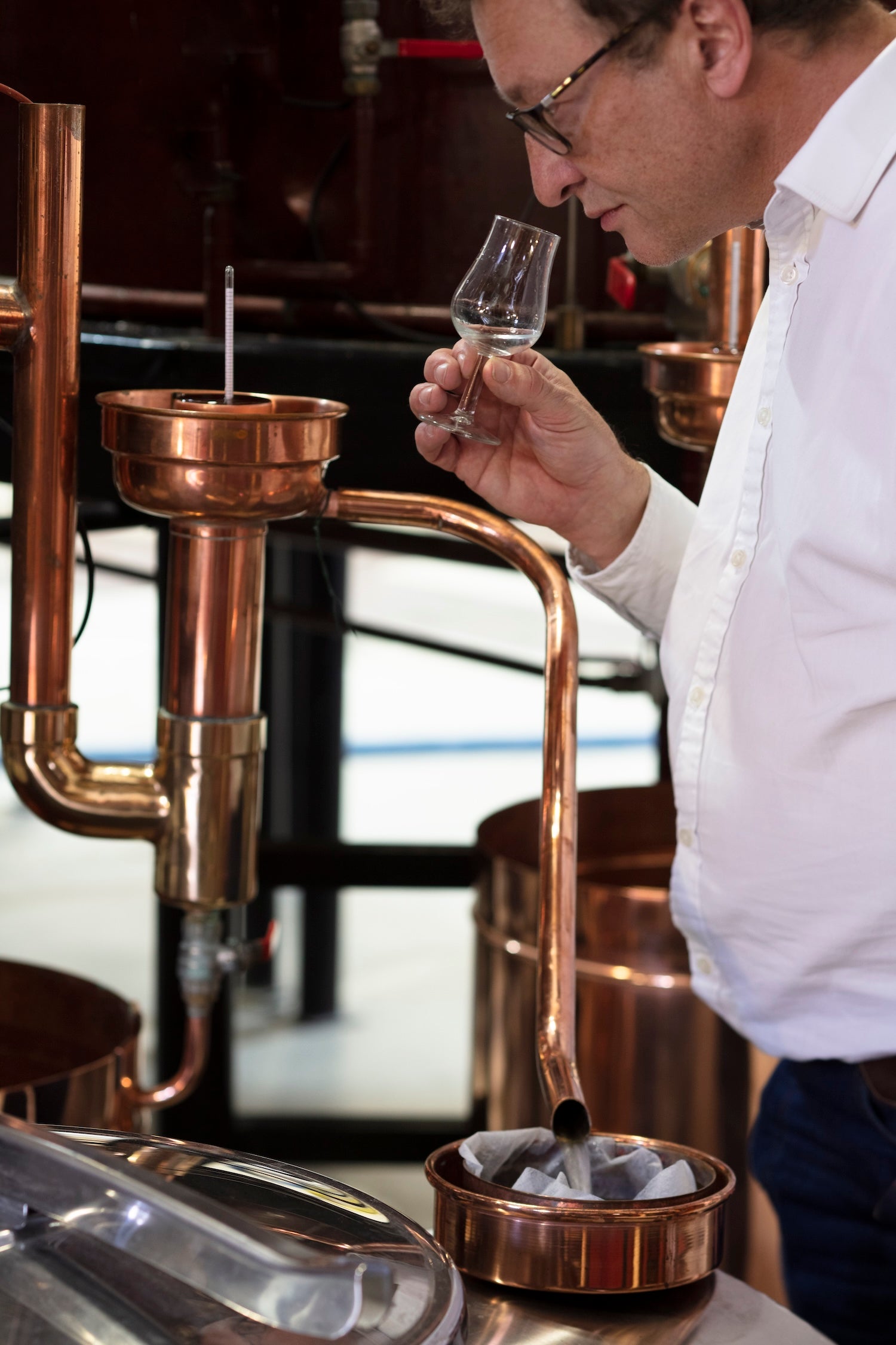 Pierre Solignac tasting a small glass of vodka in front of copper brewing equipment